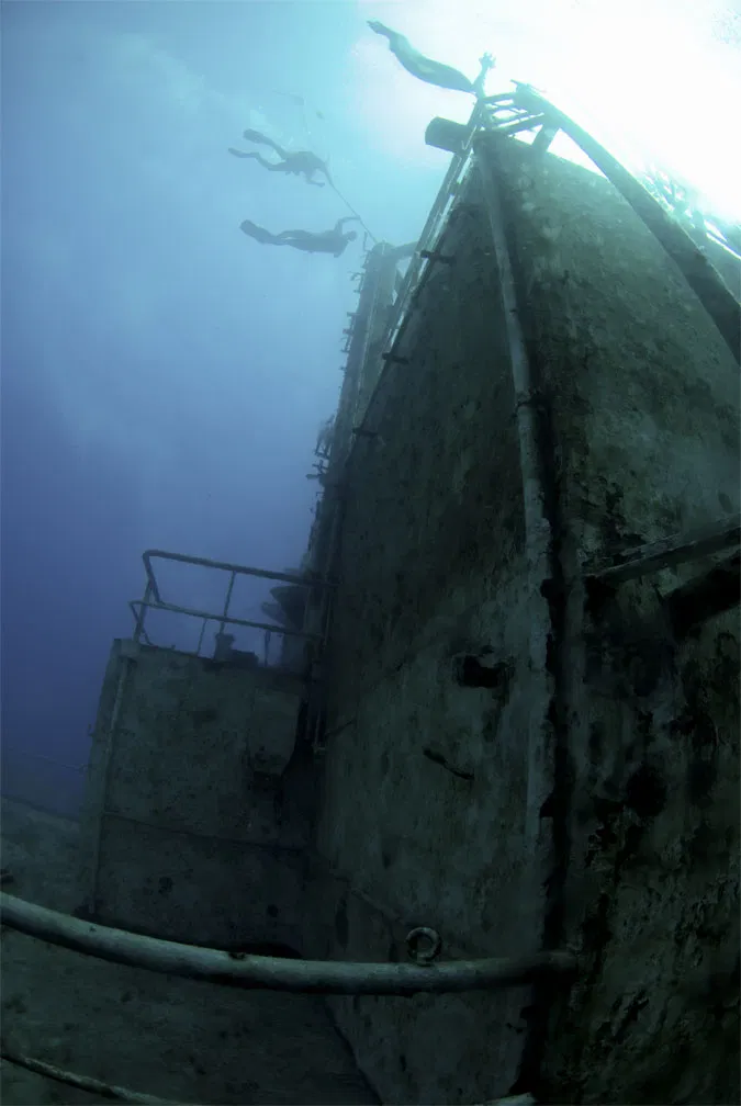 Looking up the hull of a sunken vessel with divers silhouetted against the surface light.