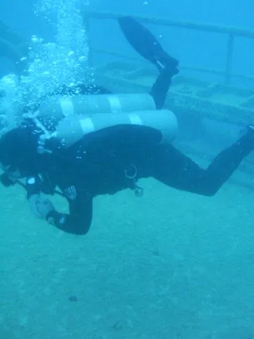Technical diver in a twinset configuration finning along a wreck at depth.