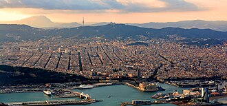 Aerial view of Barcelona at dusk, the Eixample grid running to the Mediterranean, Montjuïc and the port to the right.
